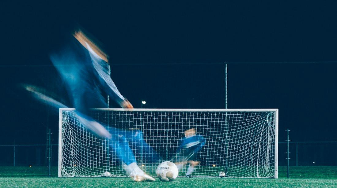 Fußballspieler beim Torschuss unter Flutlicht, schwarz-weiß