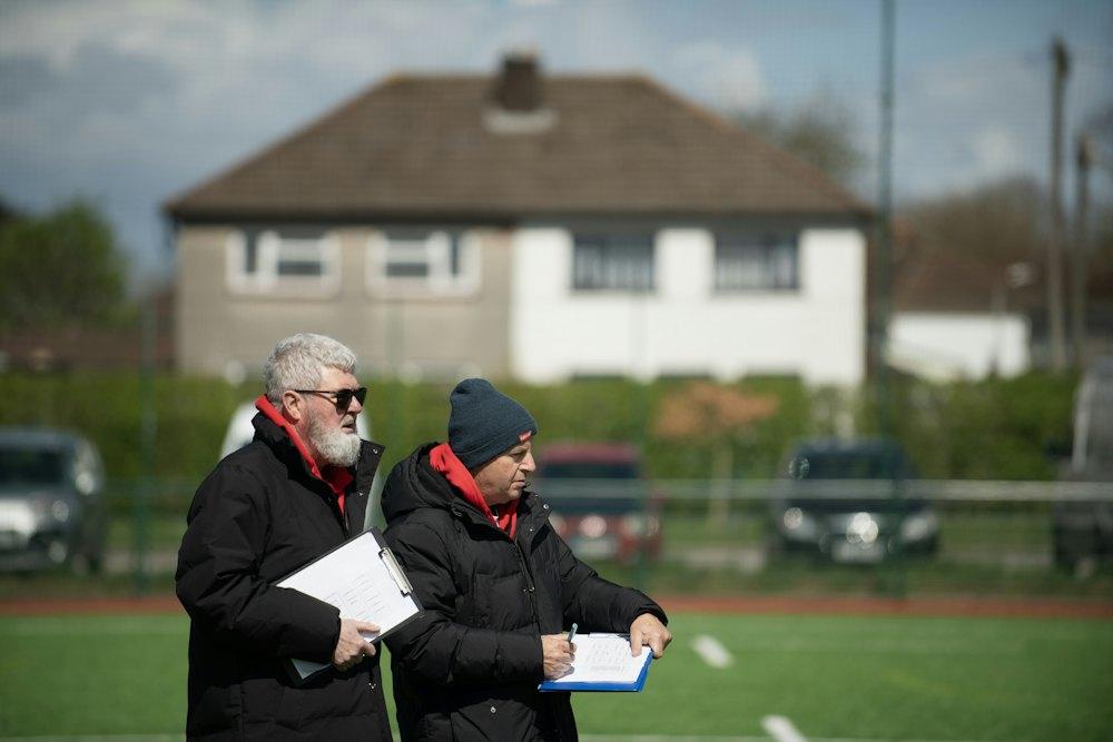 Zwei Trainer stehen nebeneinander am Spielfeldrand und machen sich Notizen